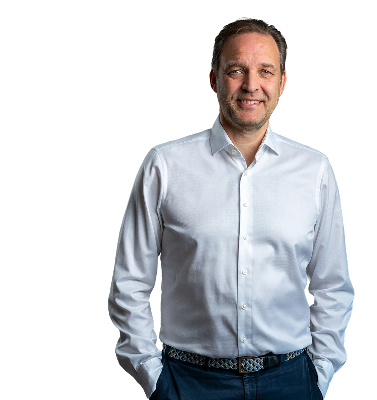 Professioneller Mann im weißen Hemd Ein lächelnder Mann steht mit beiden Händen in den Hosentaschen. Er trägt ein weißes Hemd und eine dunkle Hose. Der Hintergrund ist schwarz.